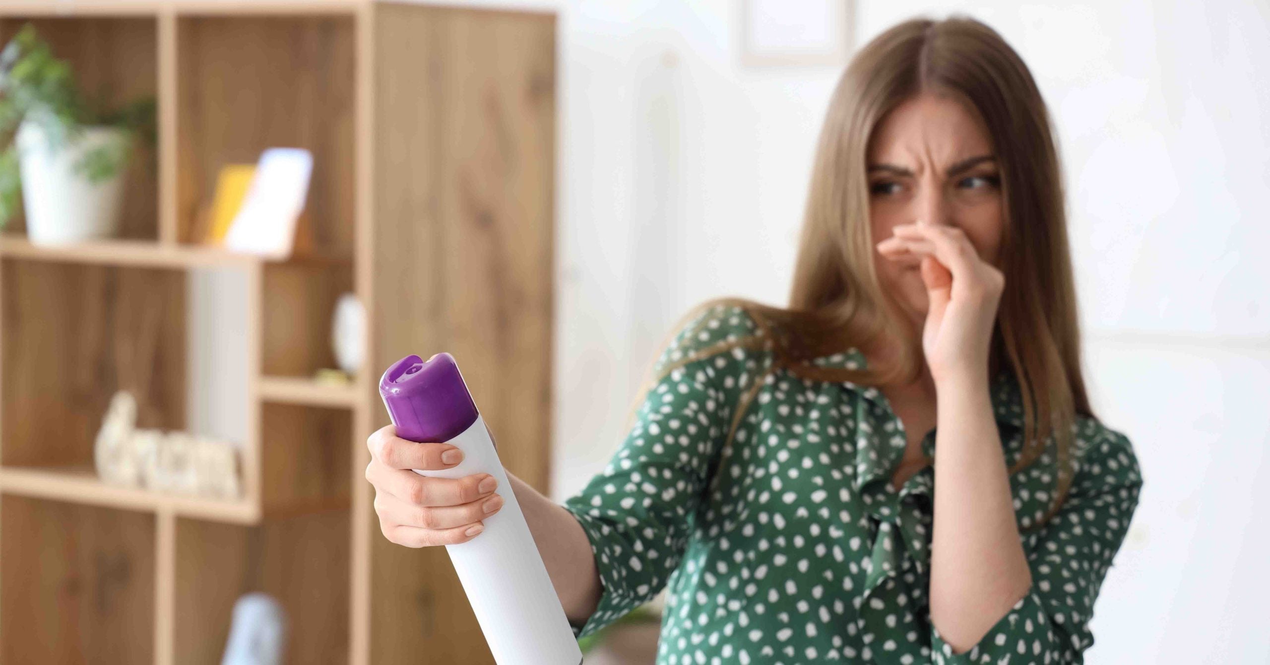 Woman spray an air freshener while holding her nose