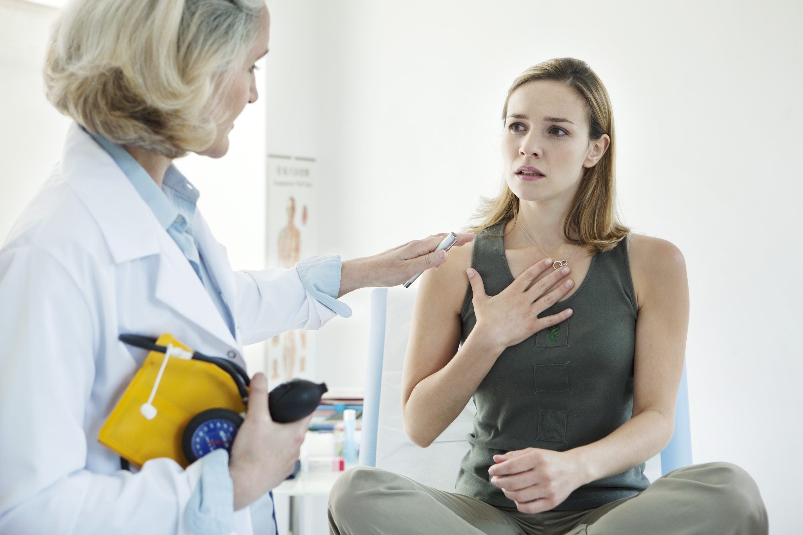 Photo of a woman sitting on doctor's exam table on the right. On the left there is a female doctor with blood pressure cuff.