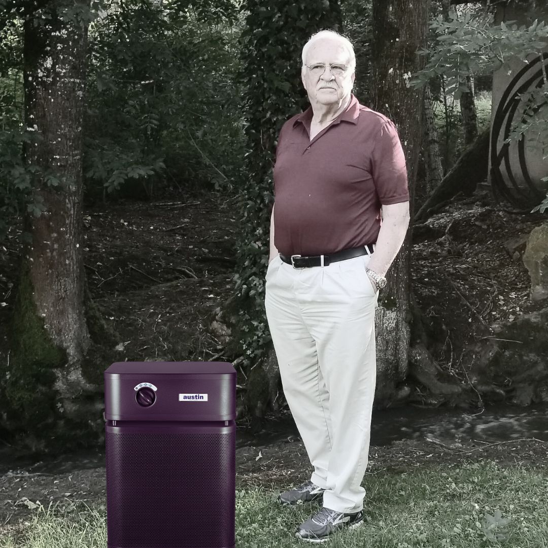Richard Taylor standing next to a black Austin Air purifier in a wooded area.