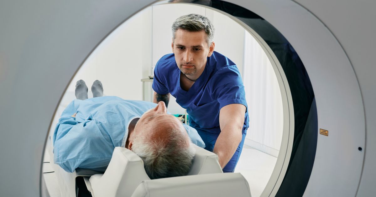 Patient in a blue hospital gown is being placed in an MRI scanner by a male medical professional 
