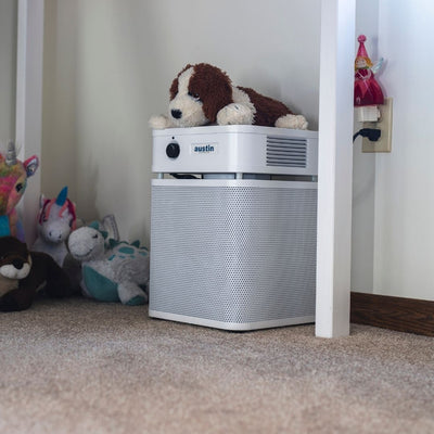 austin air healthmate plus junior air purifier with a plush dog toy on top in a room with stuffed animals.
